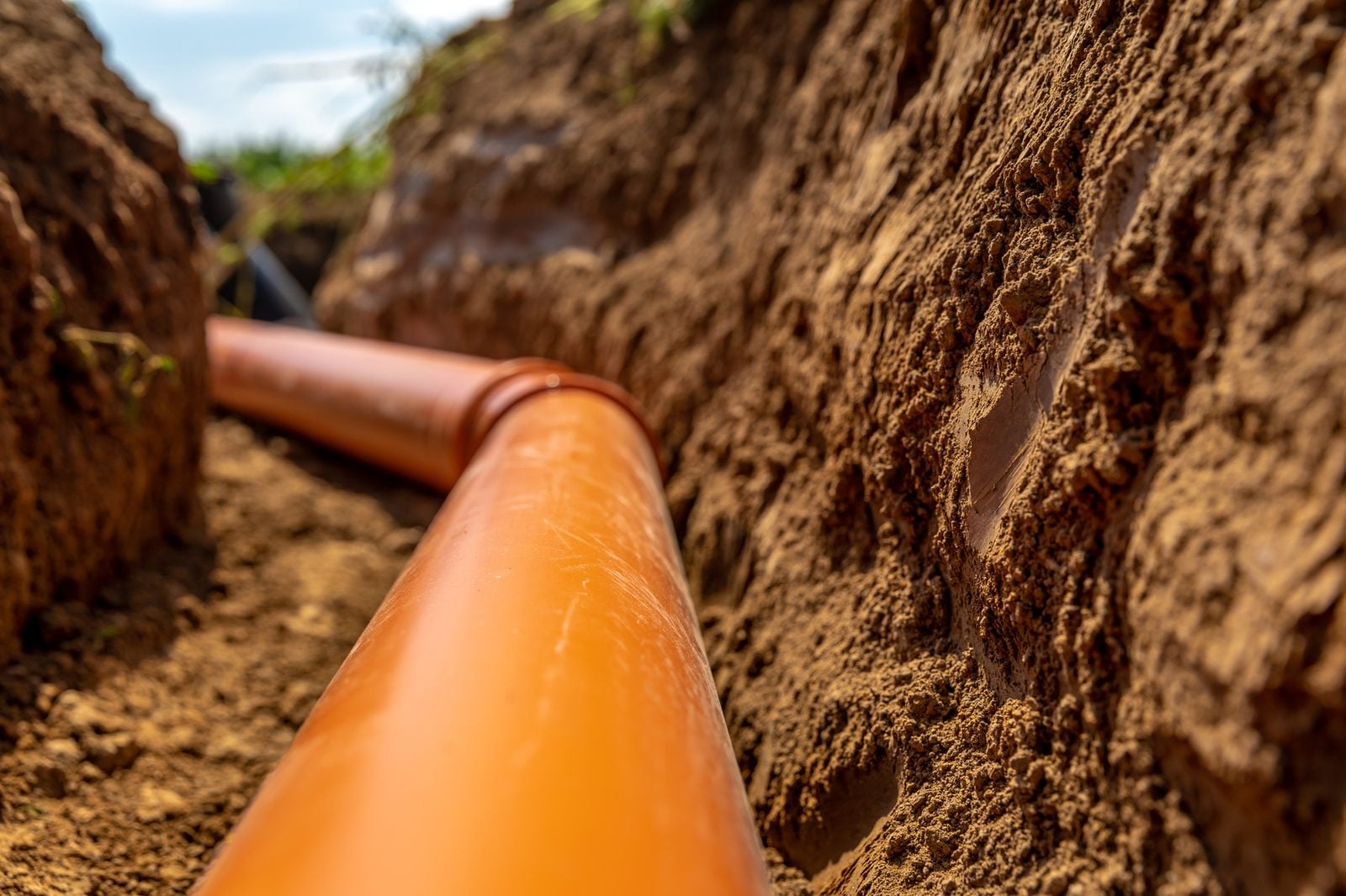 Orange sewer drain pipe laid in a dirt trench